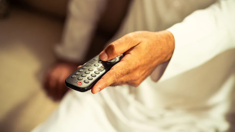 Person som byter kanal med fjärrkontroll framför TV:n